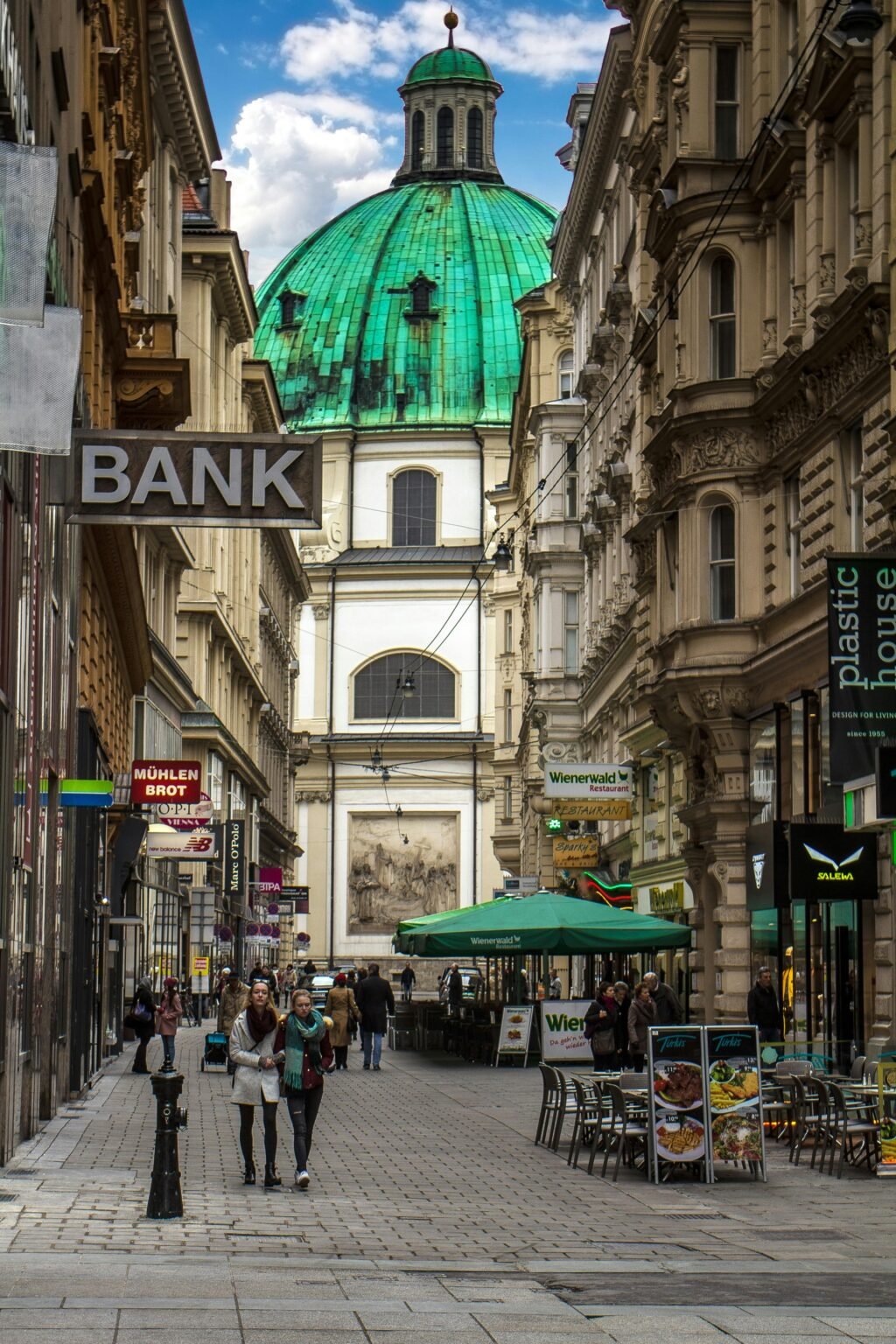 Busy pedestrian street in Vienna's historic district with view of St. Peter's Church dome.